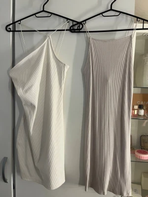 Två ribbade klänningar med smala band - Två stilrena ribbade klänningar i ljusa toner, båda med smala axelband. Den ena är kort och figurnära, den andra är längre och har en lösare passform. Perfekta för varma dagar och enkla att styla med accessoarer.