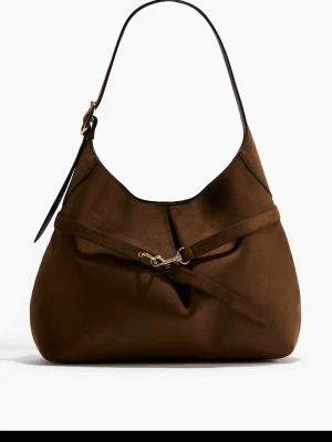 Brun axelväska i mocka från H&M - Snygg brun axelväska i mjuk mocka från H&M med justerbart axelband och dekorativt spänne i guld. Väskan har en stilren, slouchy form och svarta kanter som ger en cool kontrast. Perfekt för dig som gillar trendiga accessoarer med en lyxig känsla.