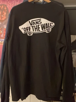 Svart loose fit sweatshirt från Vans - Cool svart sweatshirt från Vans med stort vitt 'Off The Wall'-tryck på ryggen. Tröjan har loose fit och är tillverkad i bomull. Perfekt för dig som gillar streetwear och vill ha något bekvämt och stilrent.