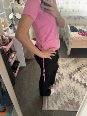 Rosa t-shirt med snörning - Säljer en rosa t-shirt med snörning i sidan. T-shirten har korta ärmar och en normal passform. Perfekt för dig som gillar en enkel men ändå unik stil. Materialet känns mjukt och bekvämt, troligtvis bomull.