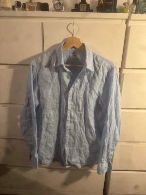 Ljusblå linneskjorta från Uniqlo - Säljer en stilren ljusblå skjorta från Uniqlo i luftigt linne. Skjortan har klassisk krage, knappar framtill och långa ärmar. Perfekt för en avslappnad men ändå snygg look. Strl xs men passar även S