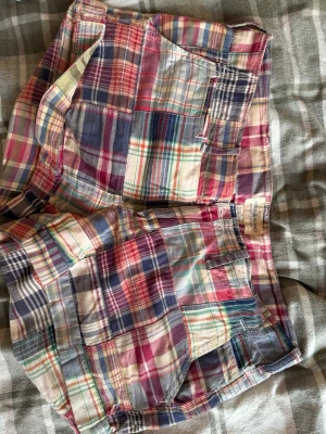 Flerfärgade rutiga shorts från Ralph Lauren  - Rutiga shorts från Ralph Lauren i flera färger. Klassisk modell med fickor fram och bak, bälteshällor och knappgylf. Tillverkade i tunn bomull, perfekta för varma dagar. Snygg retrostil som sticker ut. Pris går att diskutera vid snabbt köp. 