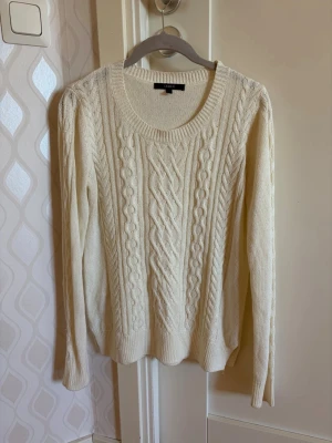 Vit kabelstickad tröja från Lindex - Snygg vit kabelstickad tröja från Lindex med rund halsringning och långa ärmar. Tröjan har klassiskt flätmönster framtill och ribbstickade muddar vid ärmslut och nederkant. Perfekt för lager-på-lager och enkel att matcha med jeans eller kjol. Ställ gärna frågor 💕