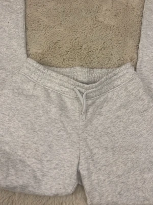 Ljusgrå mjukisbyxor med snörning - Mysiga ljusgrå mjukisbyxor med elastisk midja och snörning framtill. Byxorna har en klassisk passform och är tillverkade i mjukt bomullsmaterial. Perfekta för chill dagar eller när du vill vara extra bekväm.