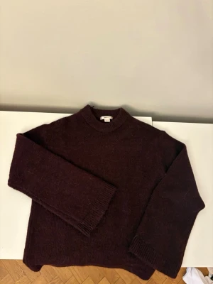 Vinröd stickad tröja från Gina Tricot - Mysig vinröd stickad tröja från Gina Tricot med rund halsringning och långa ärmar. Tröjan har en rak passform och ribbstickade muddar vid ärmslut och hals. Perfekt för kyliga dagar och enkel att matcha med jeans eller kjol.