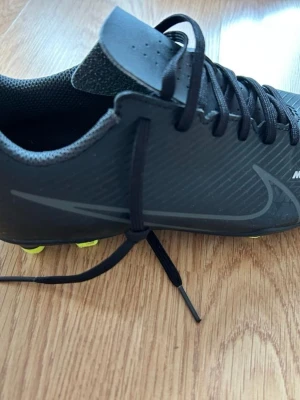 Svarta Nike Mercurial fotbollsskor - Säljer ett par svarta Nike Mercurial fotbollsskor. Skorna har låg profil, snörning och är tillverkade i syntetmaterial för bra grepp och känsla på planen. Perfekta för dig som vill ha stilrena och snabba skor på matchen. Skriv gärna vid funderingar o så. mvh!! Storleken är 36,5. Knappt använda