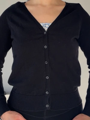 Klassisk svart H&M-kofta i ekologisk bomull, stl M – mjuk och mångsidig - Mjuk svart kofta från H&M, storlek M. 83 % ekologisk bomull, 17 % polyamid. I gott skick – perfekt till vardag eller kontor. Hämtas i Kista eller skickas.