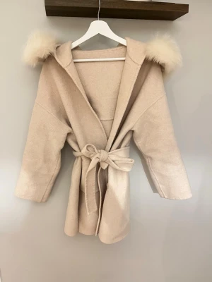 Beige kappa - Super fin Beige kappa i storlek s ifrån furstockholm med avtagbar äkta päls, kappan är i ett ullblandat tyg tyvärr är den ena tråden som ska hålla upp skärpet är sönder men går att laga annars går de att  knyta perfekt endå och inget som stör mig när jag användt kappan, en knapp vid pälsen är tyvärr bort men inget som syns heller, skriv för mer bilder !! Nypris: 2299kr 