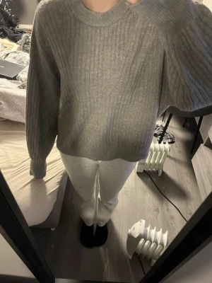 Grå ribbstickad tröja - Mysig grå stickad tröja med ribbad struktur och rund hals. Tröjan har långa ärmar och en avslappnad passform, perfekt för lager på lager. Enkel och stilren design som passar till det mesta.