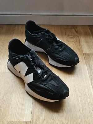 Svarta New Balance sneakers - Svarta sneakers från New Balance med vit sula och stor vit logga på sidan. Skorna har en sportig design med mesh och mockadetaljer, samt svarta skosnören. 