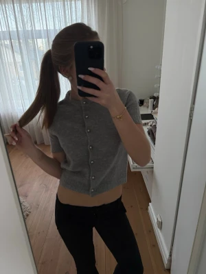 Grå kortärmad kofta med pärlknappar - Snygg grå kofta med korta ärmar och pärlknappar framtill. Modellen är croppad och har ribbade kanter vid ärmslut och nederkant. Koftan är jättebekväm kan användas till vad som!! 🤍Den är i storlek S men upplevs som XS.