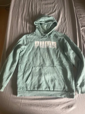 Mintgrön hoodie från Puma -  mintgrön hoodie från Puma med  vit logga på bröstet. Klassisk känguruficka framtill och huva med dragsko. Tillverkad i mjukt bomullsmaterial. Perfekt avslappnad, mys hoodie. 