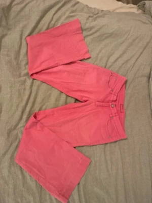 Rosa utsvängda jeans - Säljer ett par rosa jeans  med utsvängda ben och klassisk femficksmodell. Jeansen har bälteshällor, knappgylf och är tillverkade i ett mjukt bomullsmaterial. Perfekta för dig som vill sticka ut med färg och retrovibbar.
