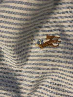 Randig skjorta från Polo Ralph Lauren - Klassisk vit och blå randig skjorta från Polo Ralph Lauren med broderad logga på bröstet. Skjortan har lång ärm, knappar framtill och breda manschetter. Tillverkad i mjuk bomull för en skön känsla och tidlös look.
