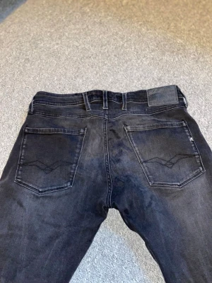 Svarta slim-fit jeans från Armani - Snygga svarta slim-fit jeans från Replay med klassiska bakfickor och diskret logotyp på ena fickan. Jeansen har en modern passform och är tillverkade i ett mjukt denim-material som ger en skön känsla. Perfekta för dig som gillar stilrena och trendiga jeans. Replay anbass strl w32 L32