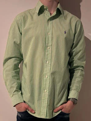Grönrandig skjorta från Ralph Lauren - Snygg grön och vit randig skjorta från Ralph Lauren med klassisk krage och knäppning framtill. ☀️Skjortan har lång ärm och en liten broderad logga på bröstet. 💯Perfekt för en stilren look. Storlek M modellen är 180 och väger 70✌️ hör av er vid minsta fråga eller fundering💯☀️✌️😊