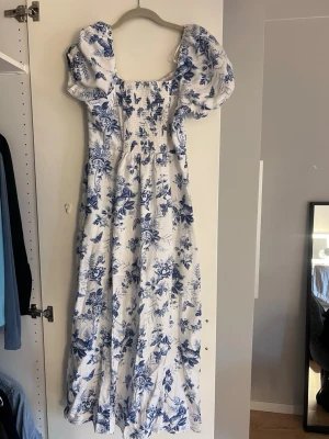 Vit och blå blommig långklänning &Other Stories - Superfin långklänning med blått blommönster på vit botten. Klänningen har puffärmar, smockad överdel och fyrkantig ringning. Materialet känns svalt och luftigt. OBS finns bus fläckar på insidan av klänningen men syns inte när klänningen är på!💞