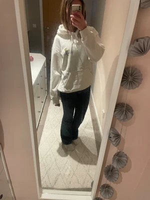 Vit hoodie med tryck och huva - Säljer en oversized vit hoodie med tryck på bröstet och ett större motiv på ryggen. Hoodien har en stor huva och känguruficka framtill. Perfekt för en chill och avslappnad stil. Materialet känns mjukt och skönt mot huden.