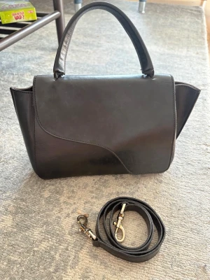 ATP atelier väska  - Svart ATP atelier väska i den stora/mellan modellen som heter Arezzo leather handbag. Nypris runt 5000 kr. Väskan är väl använd och har många repor på sig, samt att handtaget dippar och inte står upp av sig själv (Andra bilden). Därav det billiga priset. Pris går att diskutera!💕