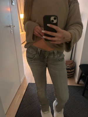 Grå low waist jeans med raka ben - Säljer ett par grå low waist jeans med raka ben och slitna detaljer. Jeansen har klassiska fem fickor och dubbla knappar i midjan. Perfekta för en avslappnad och trendig look.