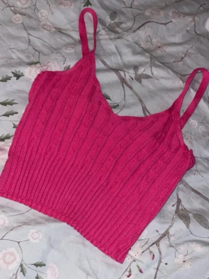 Rosa ribbad stickad linnetopp - Snygg rosa stickad linnetopp med smala axelband och ribbade detaljer. Toppen har en croppad passform och är perfekt för varma dagar. Materialet är mjukt och stretchigt vilket gör den superbekväm.