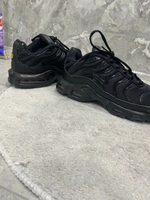 Nike Air Max Plus helsvarta sneakers - Säljer ett par helsvarta Nike Air Max Plus sneakers med synlig Air-enhet i sulan och vågiga detaljer på ovandelen. Skorna har en mix av mesh och syntetmaterial, samt en liten Swoosh på sidan. Lite använda men syns som nytt. Det är lite öppet där framme men det går att limma fast enkelt 