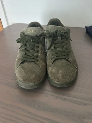 Olivgröna Polo Ralph Lauren sneakers - Snygga olivgröna sneakers från Polo Ralph Lauren i mocka med matchande gröna skosnören och diskret logga på sidan. Klassisk låg modell med rund tå och gummisula. Perfekta för en stilren och avslappnad look.