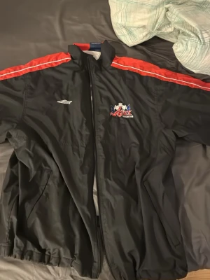 Svart Ajax windbreaker 90 tal - Säljer en svart windbreaker från fotbollsklubben Ajax från 90 talet! Dragkedjan har åkt av men lätt att sätta dit en ny