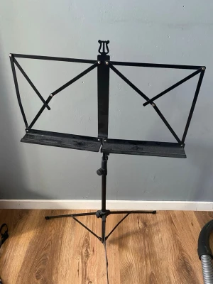Svart notställ i metall - Säljer ett svart notställ i metall med justerbar höjd och hopfällbar design. Perfekt för att hålla noter eller papper på plats under spelning eller övning. Stället har tre ben för stabilitet och en klassisk, enkel form.