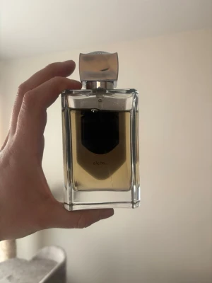 Lattafa Liam Grey - Elegant parfym från Lattafa i en rektangulär glasflaska med silverfärgat lock. Flaskan har en transparent design som visar den ljusgula vätskan inuti och en svart etikett på framsidan. Perfekt för dig som gillar stilrena och moderna doftflaskor.