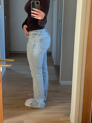 Ljusblå raka jeans med hög midja - Säljer ett par ljusblå jeans med rak passform och hög midja. Klassisk femficksmodell och stängs med dragkedja och knapp. Jeansen har en tidlös look och är tillverkade i denim, perfekt för en avslappnad stil. Innerbenslängd: 83 cm (med slits) Innerbenslängd: 72 cm (där slitsen börjar) Detta är fördelaktigt då jeansen passar olika långa ben beroende på om slitsen ska ligga över foten eller inte!