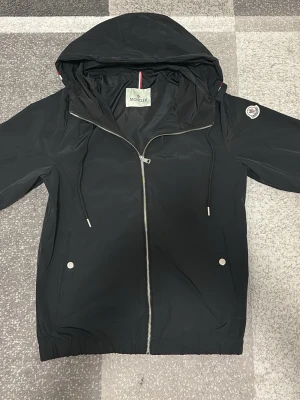 Moncler windbreaker svart - En skön moncler windbreaker i svart färg, perfekt för våren och sommaren.