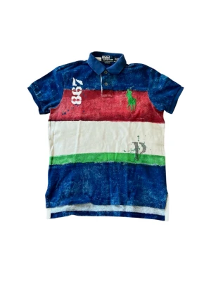 Randig pikétröja Ralph Lauren - Säljer en färgstark pikétröja från Ralph Lauren med breda ränder i blått, rött, vitt och grönt. Materialet är mjuk bomull och den har en broderad grön logga på bröstet samt siffran 837 tryckt på axeln. Perfekt för dig som vill sticka ut!