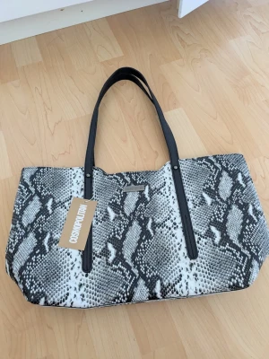 Axelväska - Snygg axelväska med svartvitt ormmönster och svarta axelband. Väskan har en rymlig insida med innerfack och dragkedja samt magnetknäppning. Nypris 390 tror jag☺️