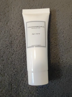 Tromborg Lip Cure läppbalsam - Tromborg Lip Cure är ett lyxigt läppbalsam i en vit tub med minimalistisk design. Tuben är gjord av plast och har en praktisk skruvkork. Perfekt för att återfukta och vårda torra läppar med en stilren look.
