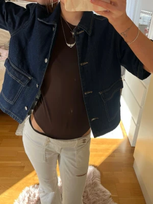 Kortärmad jeansjacka  - Säljer en mörkblå oversized jeansjacka med korta ärmar och stora fickor framtill. Jackan har klassisk krage, vita knappar och kontrastsömmar som ger en cool vintagekänsla. Perfekt att slänga över en t-shirt för en avslappnad look.
