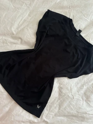 Svart sportig topp  - Snygg svart topp med rund halsringning och korta ärmar. Tillverkad i ett lätt och stretchigt material som passar perfekt till träning. Liten logga nere vid fållen och diskreta meshdetaljer vid halsen för extra ventilation.