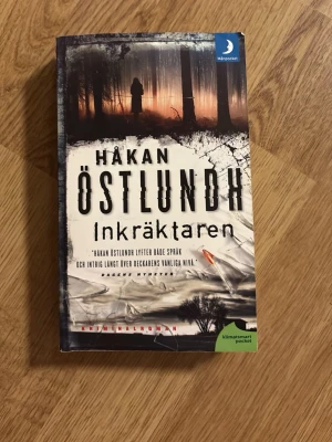 Inkräktaren av Håkan Östlundh - Spännande kriminalroman av Håkan Östlundh, pocketutgåva från Månpocket. Omslaget har en mörk och mystisk design med siluett i skog och karta över Gotland på insidan. Perfekt för dig som gillar deckare och spänning. Femte delen i Östlundhs serie om kriminalpolisen Fredrik Broman