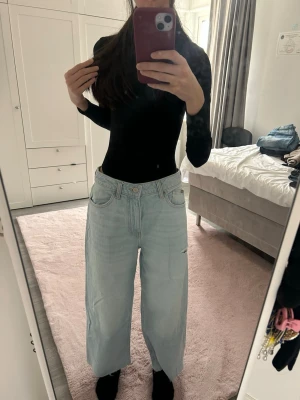 Ljusblåa vida jeans med hög midja - Säljer ett par ljusblåa jeans med hög midja och breda, raka ben. Jeansen har klassisk femficksdesign och är tillverkade i denim. Perfekta för en avslappnad och trendig look.