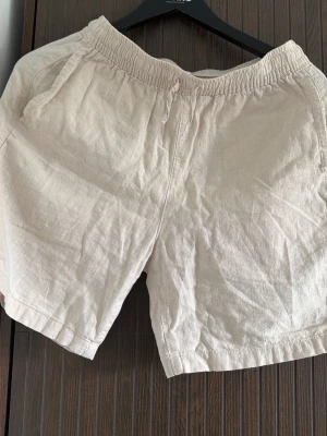 Beige linneshorts med resårmidja - Snygga beige shorts i linne med avslappnad passform och elastisk midja. Perfekta för varma dagar och har praktiska sidofickor. Lätta att matcha med olika stilar och ger en chill vibe.