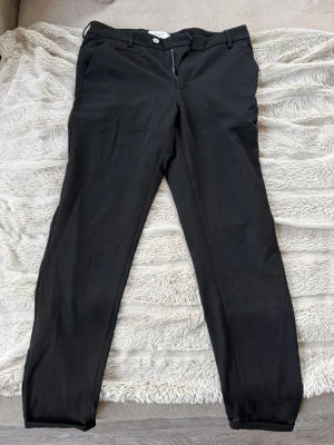 Svarta kostymbyxor från Les Deux - Snygga svarta kostymbyxor från Les Deux med klassisk rak passform och bälteshällor. Byxorna har diskreta sidofickor och stängs med dragkedja och knapp. Perfekta för en stilren look och funkar till många olika outfits.