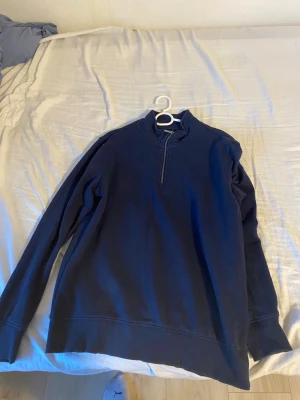 Mörkblå halvzip tröja Strömberg - Mörkblå långärmad tröja från Strömberg i mjuk bomull. Tröjan har en halv dragkedja framtill och ribbade muddar vid ärmslut och nederkant. Perfekt för en avslappnad och stilren look.