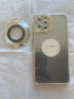 2st Glittrigt silvrigt skal till iPhone 12 Pro nya! - Snyggt mobilskal till iPhone 12 Pro i glittrigt silver med guldfärgade kanter och en kameraram dekorerad med små stenar för extra bling. Skalets material är hårdplast och det medföljer en matchande ringhållare. Perfekt för dig som vill sticka ut med din mobil! Den andra är transparent med guldkanter. Båda nya!