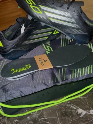 Adidas X Speedflow fotbollsskor svart/neon - Säljer ett par Adidas X Speedflow fotbollsskor i svart med neon- och silverdetaljer. Skorna har klassiska tre ränder på sidan, låg profil och snörning. Medföljer komfortsulor och en matchande svart väska med neonfärgade detaljer. Perfekta för snabba spelare!
