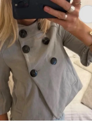 Ljusgrå trekvartsärm kappa - Trendig ljusgrå kappa med kortare passform från Zara Basic. Kappan har stora svarta knappar i dubbelknäppt design, trekvartsärmar och två fickor framtill. Första bilden är Lånad från tjejen jag köpte av. Jättefin men tyvärr för liten för mig!skriv vid funderingar 💗💗