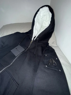 Moose Knuckles Bunny - Snygg svart hoodie från Moose Knuckles med dragkedja, vit fluffig foder i huvan och logga på ärmen. Passar för nu. Väldigt bekväm att ha på sig. Man kan ta av pälsen på den. Pris kan diskutera 