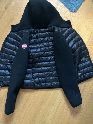 Svart pufferjacka från Colmar BYTE GÅR OCKSÅ - Säljer en svart pufferjacka från Colmar Originals med huva och vadderade paneler. Jackan har svarta ärmar i mjukt material och klassisk Colmar-logga på ena ärmen. Perfekt för kalla vinterdagar och riktigt snygg streetstil.