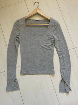 Grå långärmad topp med rund hals - En enkel och stilren grå långärmad topp med rund, djup ringning. Tillverkad i ett mjukt och stretchigt material som sitter tajt mot kroppen. Perfekt att matcha med jeans eller kjol för en clean look.