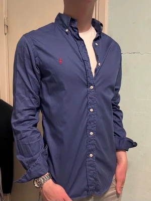 Blå Ralph Lauren skjorta – M Slim Fit - Säljer denna stilrena och snygga blåa Ralph Lauren skjorta. Skjortan är i  hyfsat bra skick. Modellen är M slim fit. Har du några frågor? Tveka inte att höra av dig. Allt gott från Deluxe garderoben ⭐️