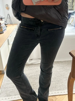 Svarta jeans med dragkedjedetaljer - Snygga svarta jeans med raka ben och coola dragkedjor framtill vid fickorna. Jeansen har en klassisk femficksmodell och är tillverkade i ett stretchigt denimtyg som sitter bekvämt. Perfekta för dig som gillar en stilren men edgy look. Passar ca 38❤️ 